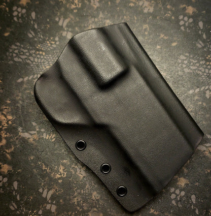 Black holster on a textured surface, featuring an ergonomic design and three metal grommets for attachment.