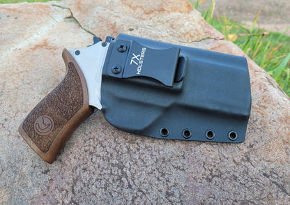 A sleek black holster with a silver and wooden grip knife on a textured rock surface, showcasing its design and clip feature.