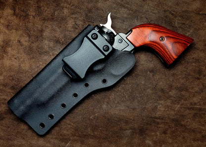 A revolver with a wooden grip rests in a black holster, showcasing its sleek design against a textured brown background.