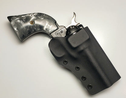 A metallic revolver is partially housed in a sleek black holster, resting on a light surface.